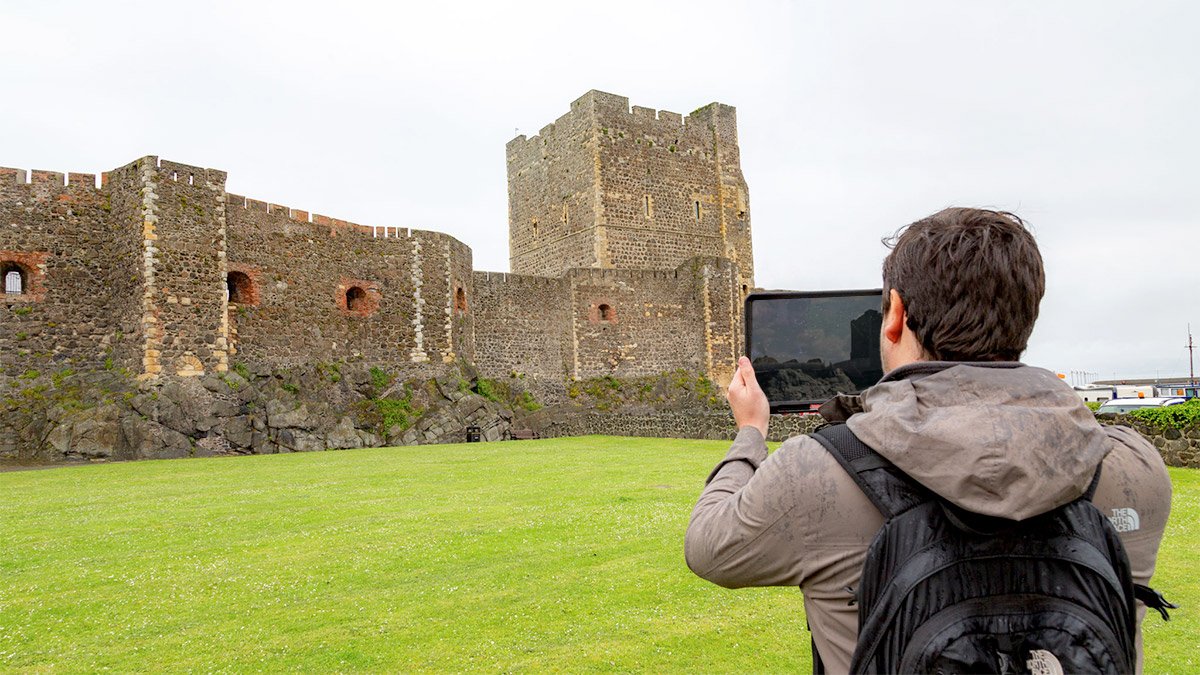 Person holding iPad testing immersive AR heritage site reconstruction app for Carrickfergus Castle, Tourism Northern Ireland