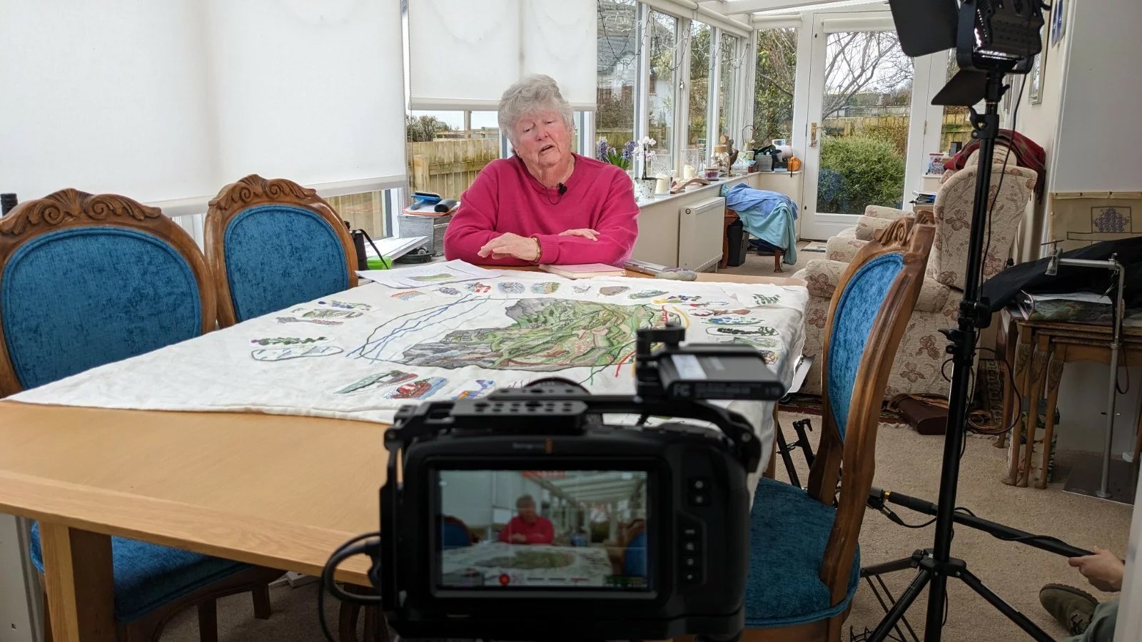 Woman talking to camera, showing the tapestry she is working on for the Digital Tapestry of the Scottish Highlands and Islands project