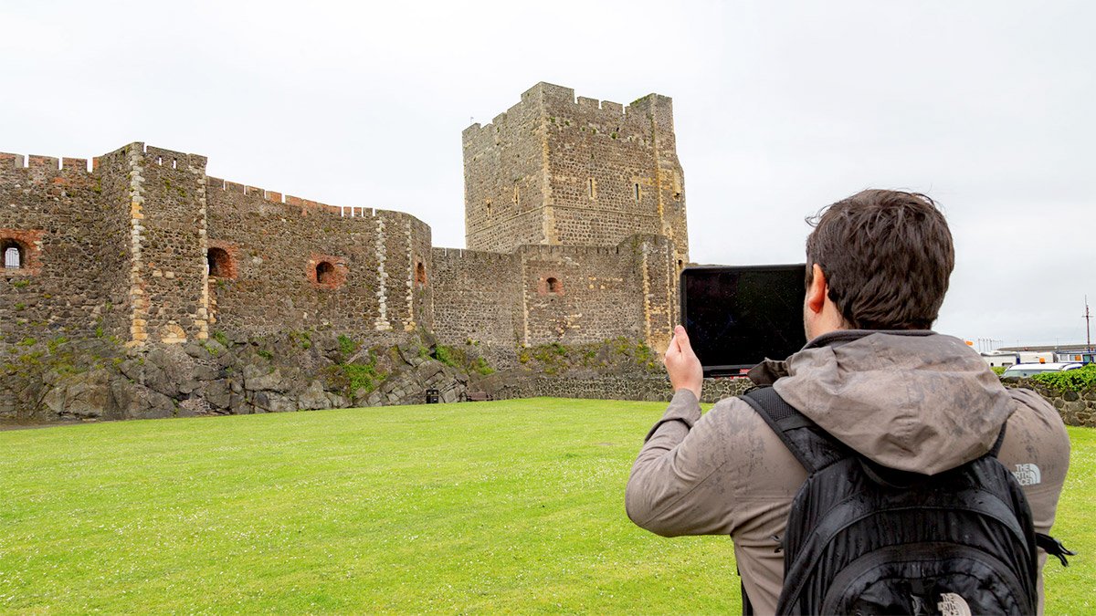 Person holding iPad testing immersive AR heritage site reconstruction app for Carrickfergus Castle, Tourism Northern Ireland