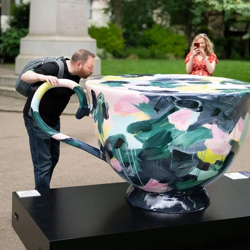 A man posing for a photo beside a mug sculpture featured in the London Heritage AR Trail.