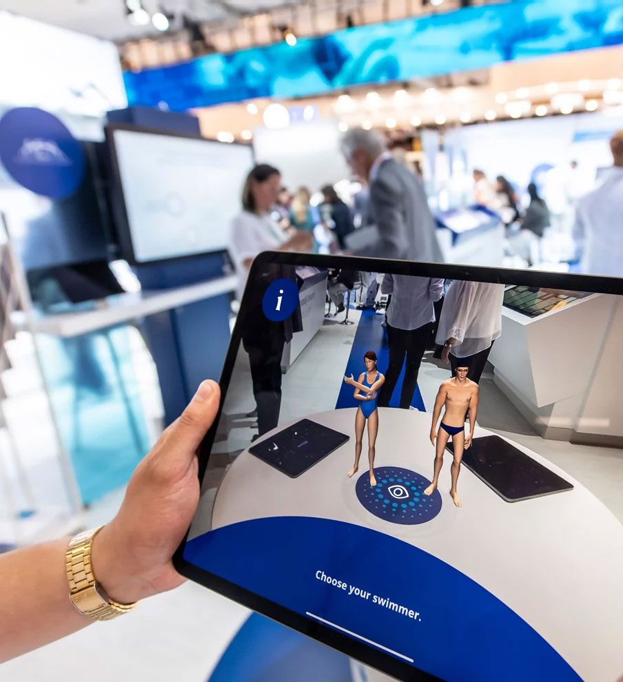 Person holding an iPad with an Augmented reality app with two swimmers for medical exhibitor